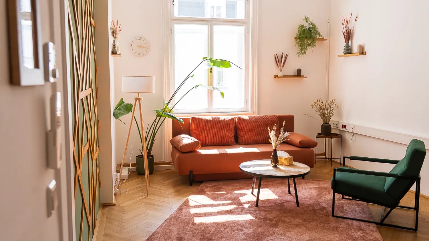 Heller Therapieraum mit orangem Sofa, grünem Sessel und rundem Tisch vor einem hohen Altbaufenster.