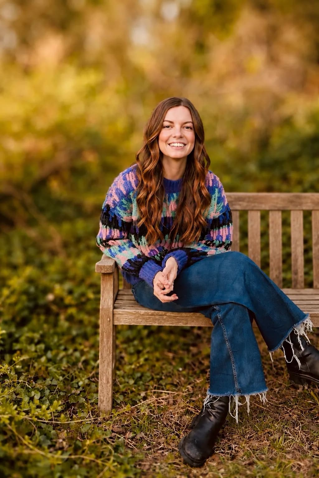 Sophie Bruckner sitzt lächelnd auf einer Holzbank im Grünen, im bunten Strickpullover.